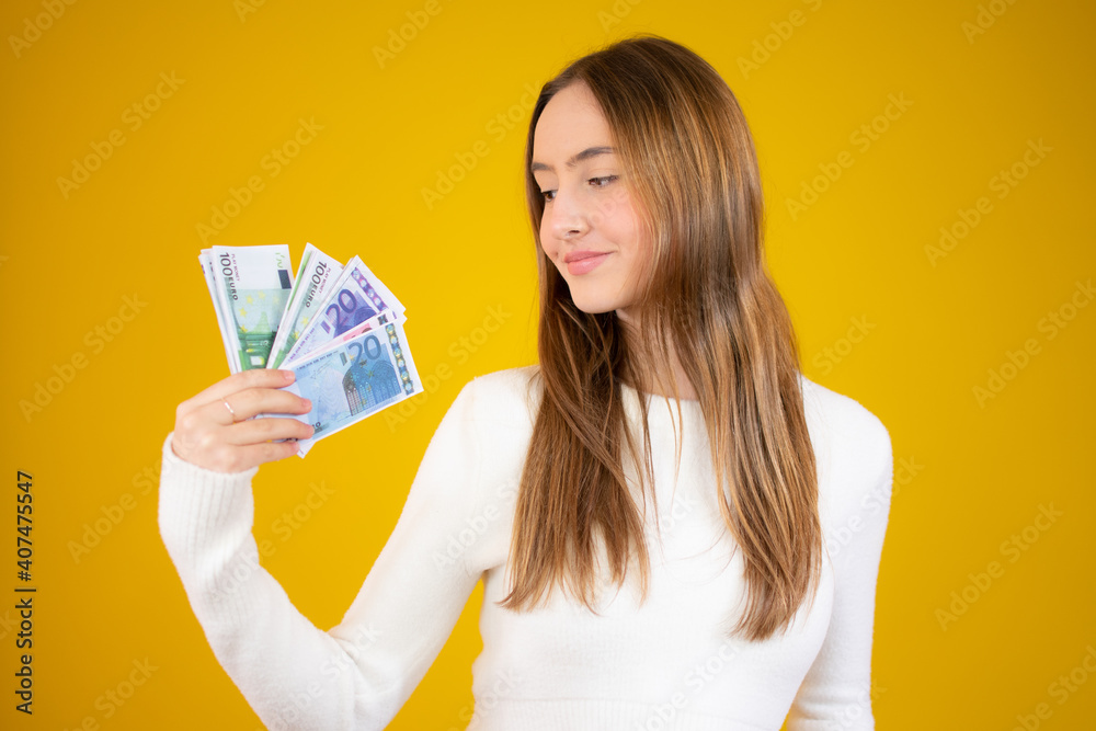 Young beautiful caucasian girl holding money over yellow background Young beautiful caucasian girl holding money over yellow background
