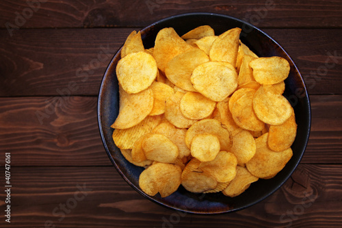 Potato chips in bowl on a wooden background, top view.