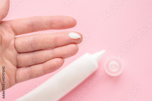 Female hand with a drop of cream on a finger. Jar, bottle, tube of cream isolated on a pink background. Antibacterial acne cream for problem skin. Сream to reduce pore tightening