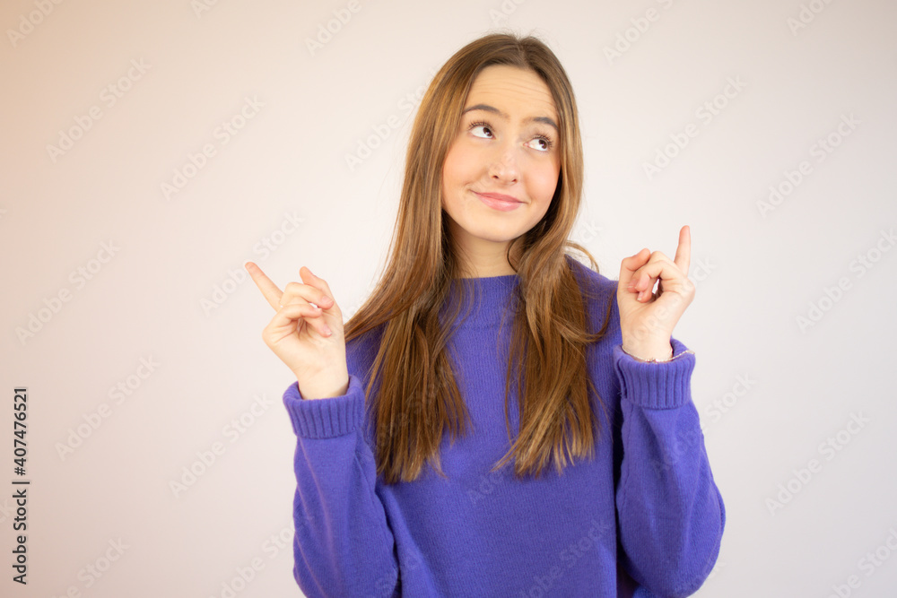 Happy beautiful young woman in lila sweater is pointing up, looking away and talking. Waist up studio shot on white background. Happy beautiful young woman in lila sweater is pointing up, looking away and talking. Waist up studio shot on white background.