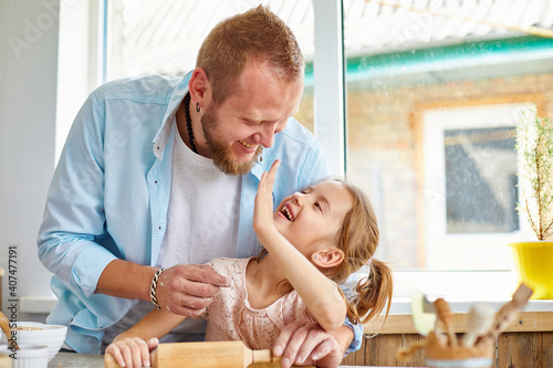 Happy family, father and daughter roll out cookie dough in a kitchen at home.