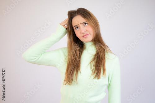 Oops, what did I do? Beautiful young girl holding hand on head with frightened and regret expression. Wearing casual clothes standing against white background.