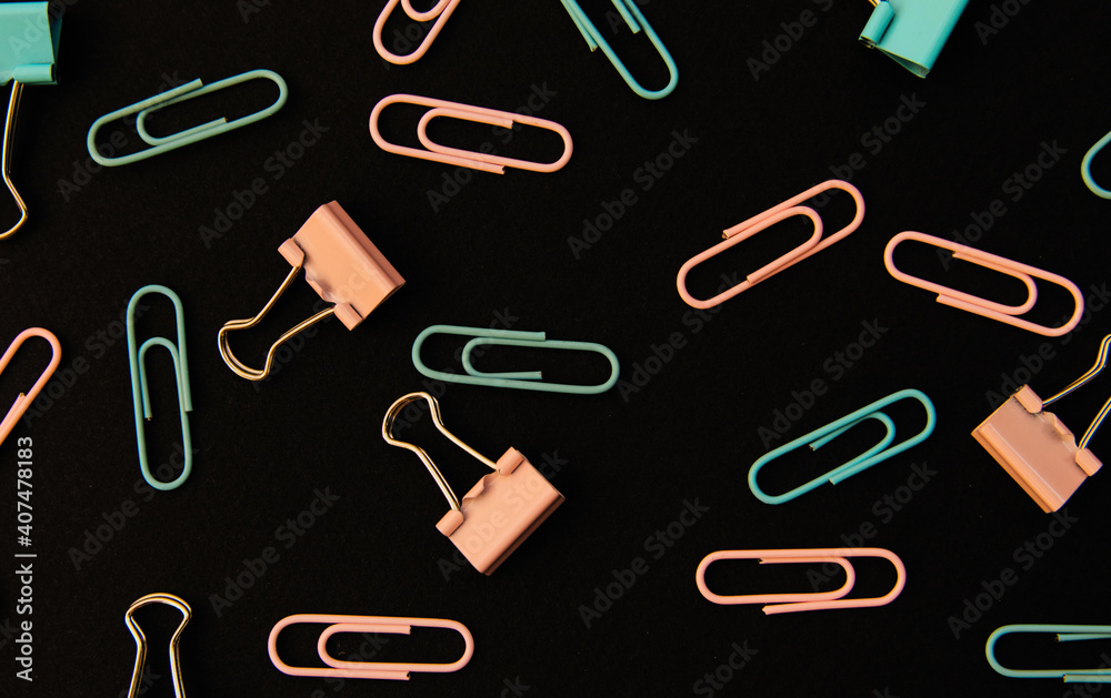 Paper clips and clips in blue and pink are scattered on a black background. Office supplies. Background and texture. Paper clips and clips in blue and pink are scattered on a black background. Office supplies. Background and texture.