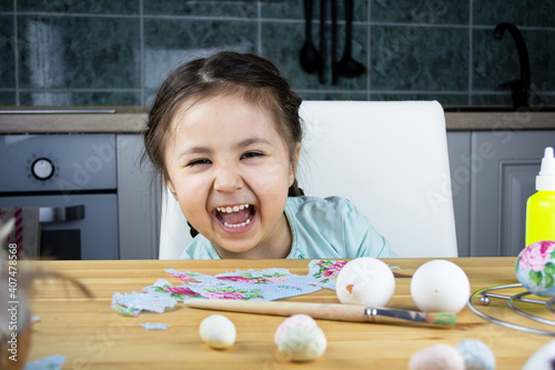 Preparing for Easter. A cute little girl sits at a table, laughs and going to decorate eggs, Decoupage on eggs for home decoration