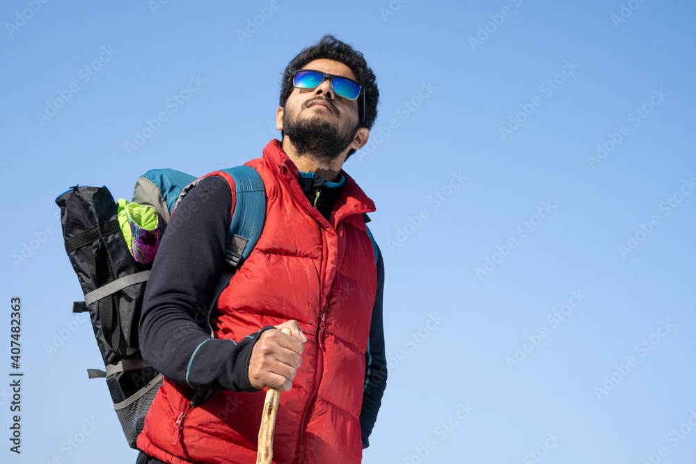 Young indian traveler boy trekking over a rocky mountain, standing on the top of the mountain with a stick in his hands. Freedom and adventure concept with copy space. Young indian traveler boy trekking over a rocky mountain, standing on the top of the mountain with a stick in his hands. Freedom and adventure concept with copy space.