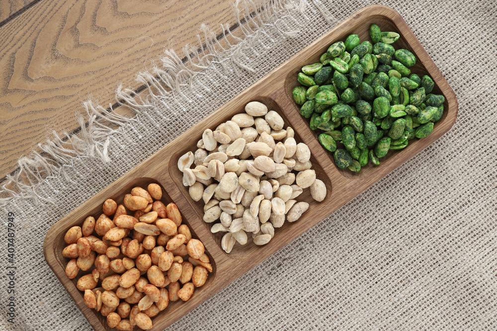 colorful roasted peanuts in a three-section wooden bowl that sits on a burlap tablecloth with