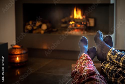 Couple sitting in front of the fireplace relaxes with the warm fire by warming their feet. Concept of winter holidays, christmas holidays and love on valentines day