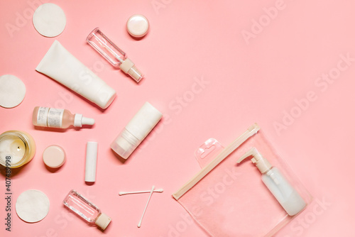 Top view flat lay with skincare goods: shampoo, deodorant, cream, facial mist, essence, serum, lipstick, balm, cotton pads and buds on a pastel pink background.