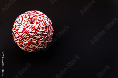 On a black background  a ball of twine is red and white. Threads for wrapping gifts.