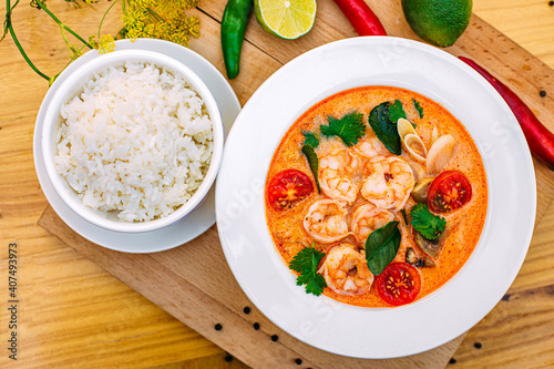 Thai soup tom yam with shrimps and tomatoes and rice as a garnish on a decorated table