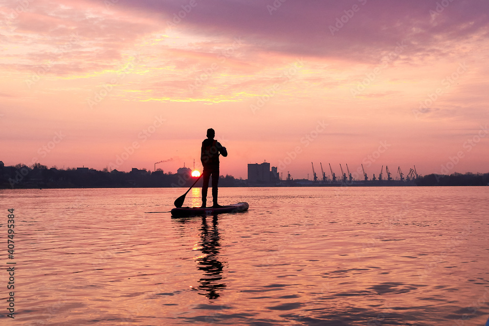 Silhouette of a young man rowing on a SUP during a beautiful winter sunrise on the river