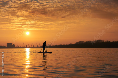 Silhouette of a boy standing on SUP during a beautiful winter sunrise on the river