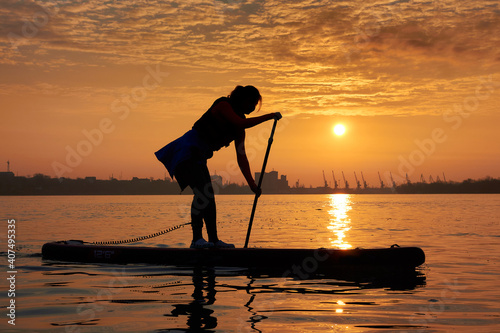 Silhouette of a young woman rowing on a SUP during a beautiful winter sunrise on the river