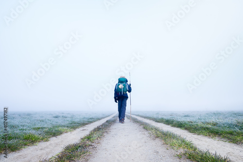 Billede på lærred A Lone Pilgrim Girl Hiker Walking off into the Frosty Morning Fog on the Way of