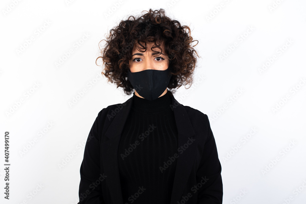 young beautiful caucasian woman wearing medical mask standing against white wall, frowning his eyebrows being displeased with something. young beautiful caucasian woman wearing medical mask standing against white wall, frowning his eyebrows being displeased with something.