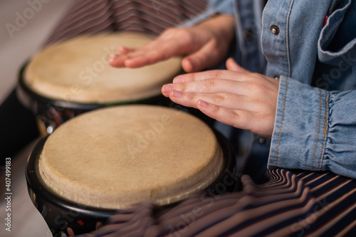 Close-up of female hands on mini bongo drums. The girl plays a traditional ethnic percussion instrument
