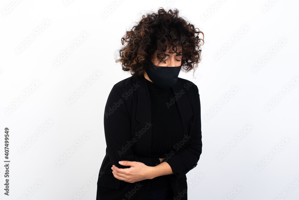 young beautiful caucasian woman wearing medical mask standing against white wall, suffering from strong stomachache. young beautiful caucasian woman wearing medical mask standing against white wall, suffering from strong stomachache.