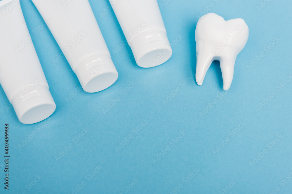 Top view of tooth model and tubes with toothpaste on blue background Top view of tooth model and tubes with toothpaste on blue background