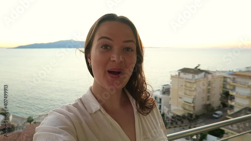 Female influencer filming happily at beachfront balcony on holiday in Greece, Europe.