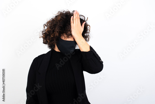 Frustrated young beautiful caucasian woman wearing medical mask standing against white wall, holding hand on forehead being depressed regretting what he did having headache, looking stressful.