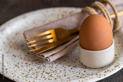 Traditional festive table setting  for festive dinner, plate with gold cutlery and  bird feathers on beige concrete background.  Happy Easter concept. photo