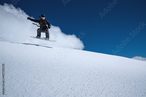 Woman athlete snowboarder in flight after jumping on a snowy slope against a background of a dark blue sky