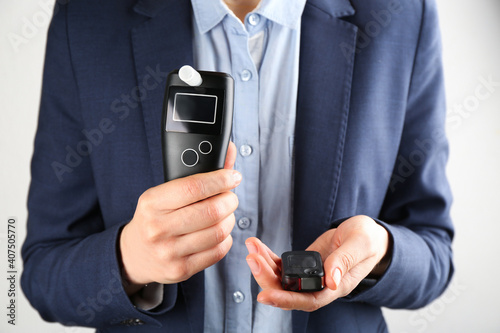 Obraz na plátně Woman holding modern breathalyzer and car key on light background, closeup