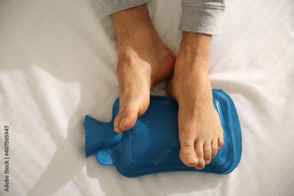 Man warming feet with hot water bottle on bed, closeup