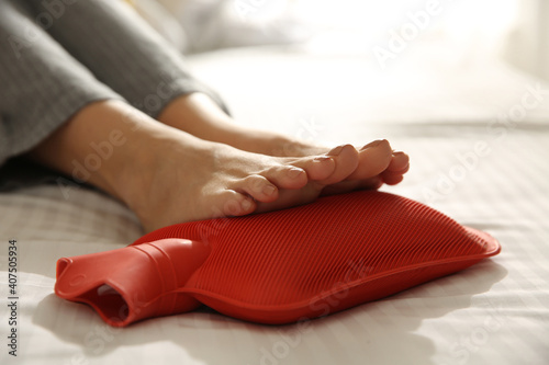 Canvas Print Woman warming feet with hot water bottle on bed, closeup