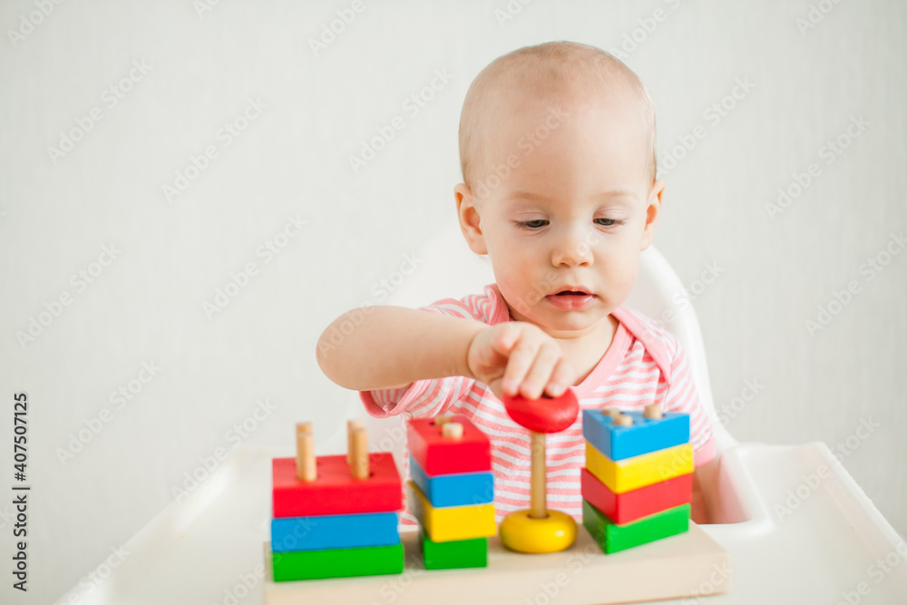 little girl plays with an educational toy - a multi-colored wooden pyramid. Development of fine motor skills and logical thinking. High quality photo little girl plays with an educational toy - a multi-colored wooden pyramid. Development of fine motor skills and logical thinking. High quality photo