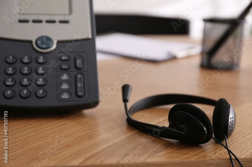 Office desktop telephone and headset on wooden table, closeup. Hotline service