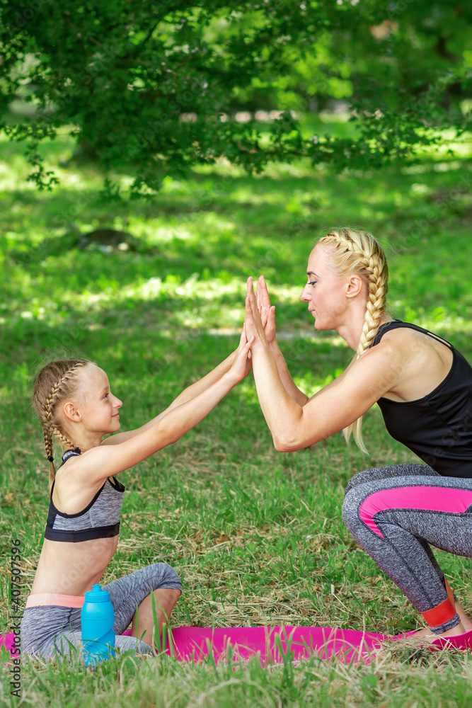 Fototapeta premium Mother and daughter doing sports exercises on the mat in the park outdoor