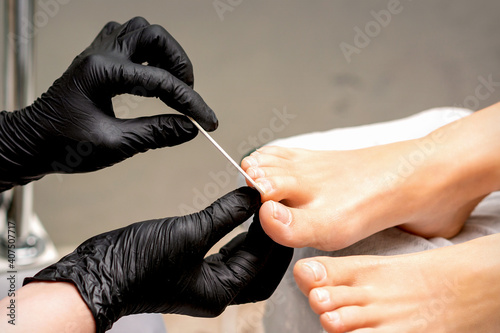 Pedicure master's hands in protective rubber gloves file female toenails with a nail file in a beauty salon
