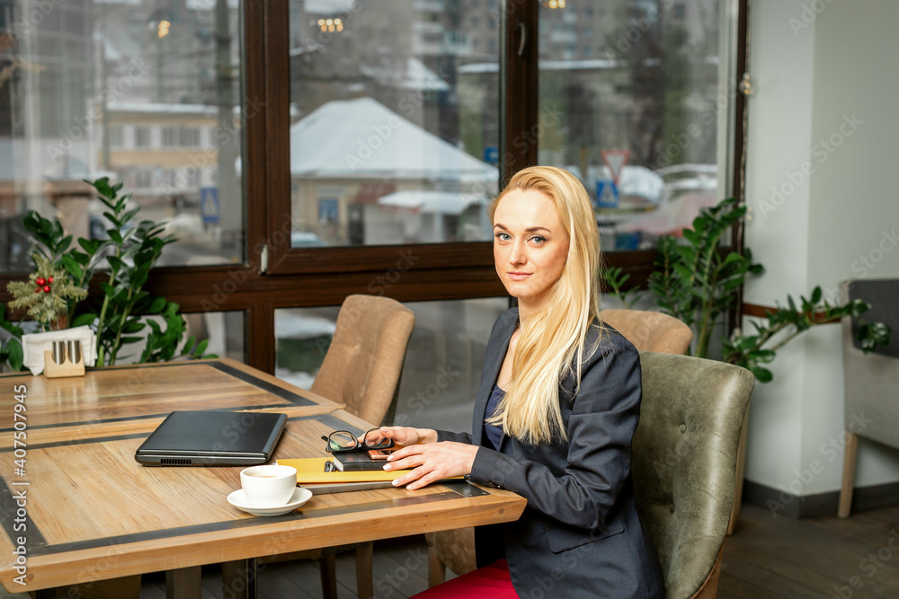 Portrait of a young caucasian businesswoman with documents and laptop at the table looking at the camera in cafe Portrait of a young caucasian businesswoman with documents and laptop at the table looking at the camera in cafe