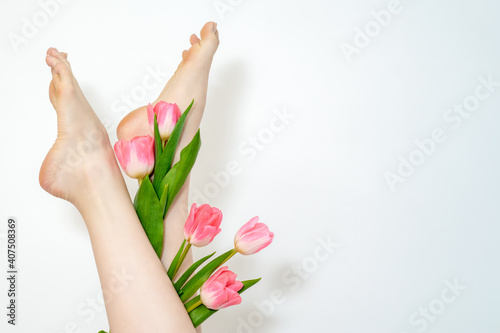 Beautiful slim smooth woman s legs with tulips flowers on white background