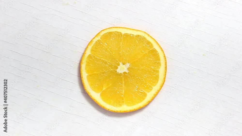 Fresh orange slice in the shape of a circle on a white background on a rotating surface. The view from the top. Fresh orange slice in the shape of a circle on a white background on a rotating surface. The view from the top.