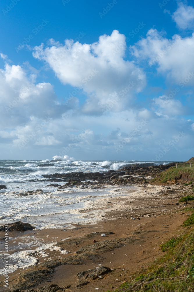 Coastline with rocks, a blue sky and rough incoming waves with sea spray during a storm Coastline with rocks, a blue sky and rough incoming waves with sea spray during a storm