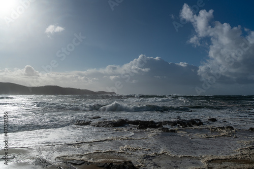 Coastline with rocks, a blue sky and rough incoming waves with sea spray during a storm