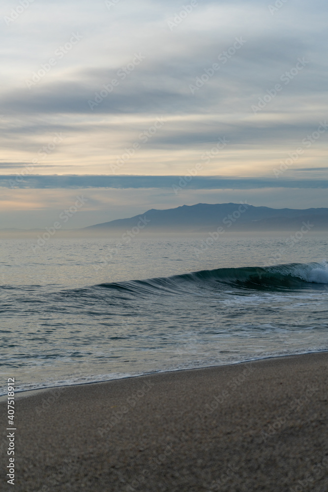 Waves breaking on a sandy beach, spray, white water and grass in foreground