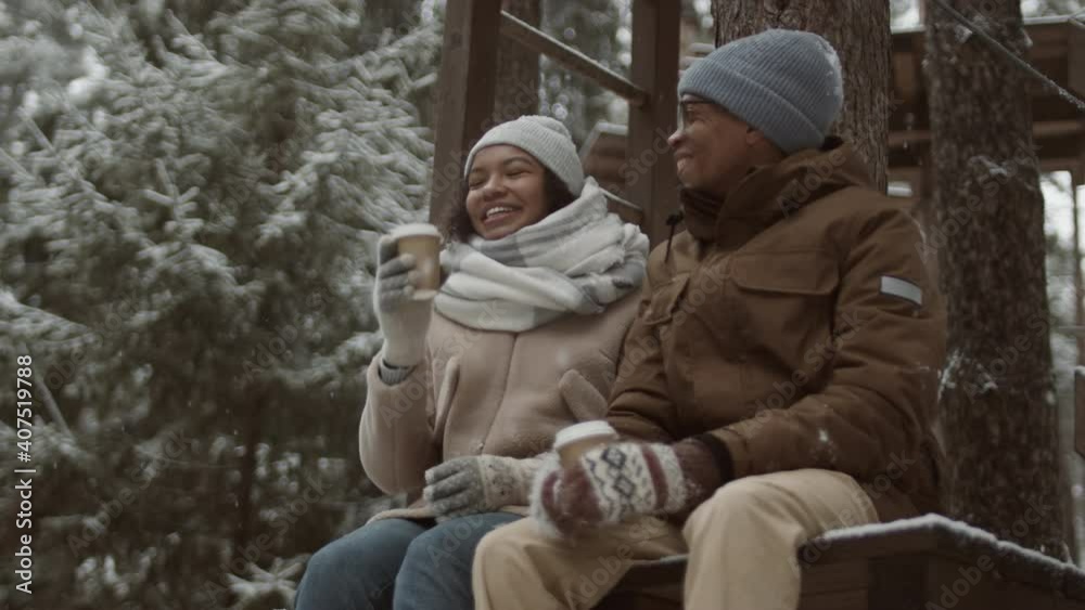 Low angle view of young mixed-race woman and her African husband sitting on bench in park, chatting and drinking hot tea Low angle view of young mixed-race woman and her African husband sitting on bench in park, chatting and drinking hot tea