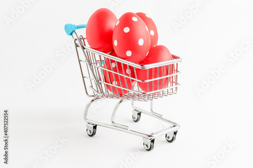 Decorative red Easter eggs in a small supermarket shopping cart isolated on a white table .