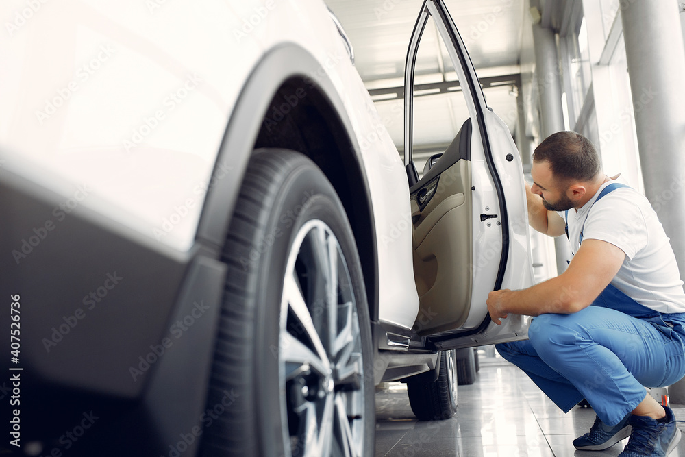 Wrker in a car salon. Expert checks the car. Man in a blue uniform. Wrker in a car salon. Expert checks the car. Man in a blue uniform.