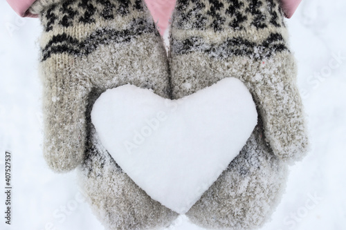 Women's hands in woolen mittens hold a snowy heart close-up. Symbol of love. Valentine's Day concept. Selective focus