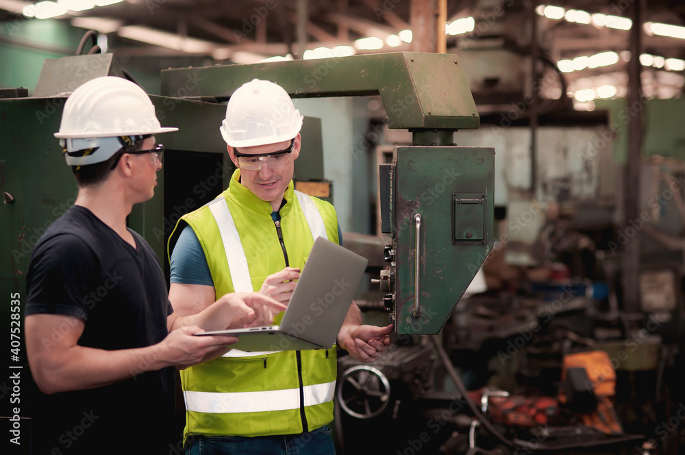 Two Caucasian Factory Technician Engineer is working with machine in industrial plants and check the operation and maintenance program of the machine in the laptop Two Caucasian Factory Technician Engineer is working with machine in industrial plants and check the operation and maintenance program of the machine in the laptop