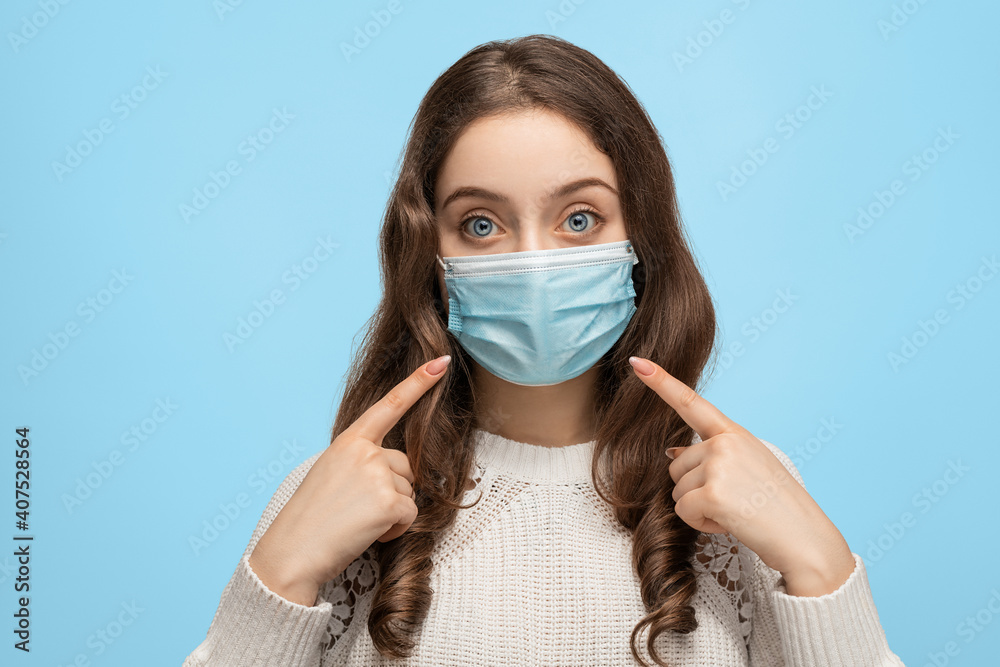 Young woman with big blue eyes in a medical mask on a blue background. Portrait of a young girl in a medical mask. Young woman with big blue eyes in a medical mask on a blue background. Portrait of a young girl in a medical mask.