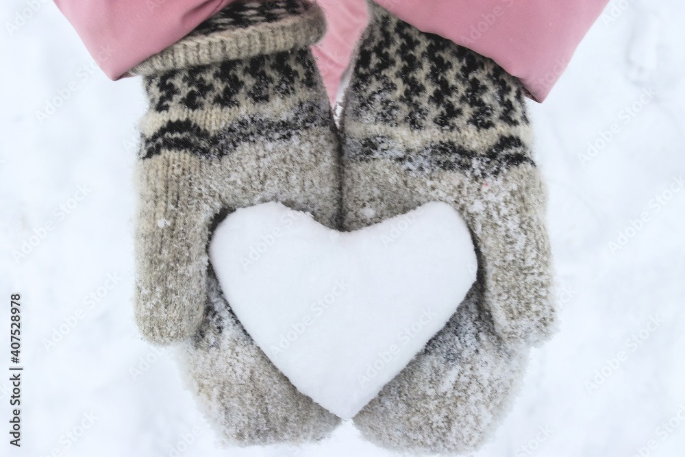 Women's hands in woolen mittens hold a snowy heart. Symbol of love. Valentine's Day concept. Selective focus, close-up