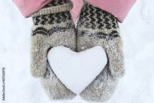 Women's hands in woolen mittens hold a snowy heart. Symbol of love. Valentine's Day concept. Selective focus, close-up
