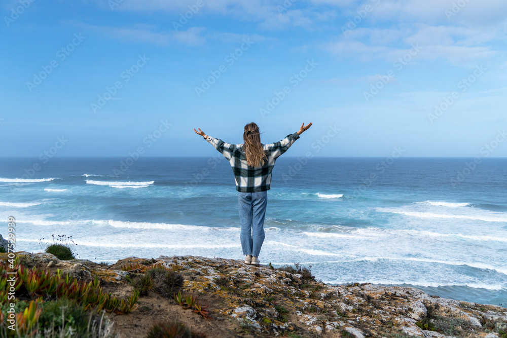 Beautiful girl looking at the sea and ocean waves on top of the beach showing happiness and joy seeking freedom. People concept, wanderlust traveling and tourism lifestyle Beautiful girl looking at the sea and ocean waves on top of the beach showing happiness and joy seeking freedom. People concept, wanderlust traveling and tourism lifestyle