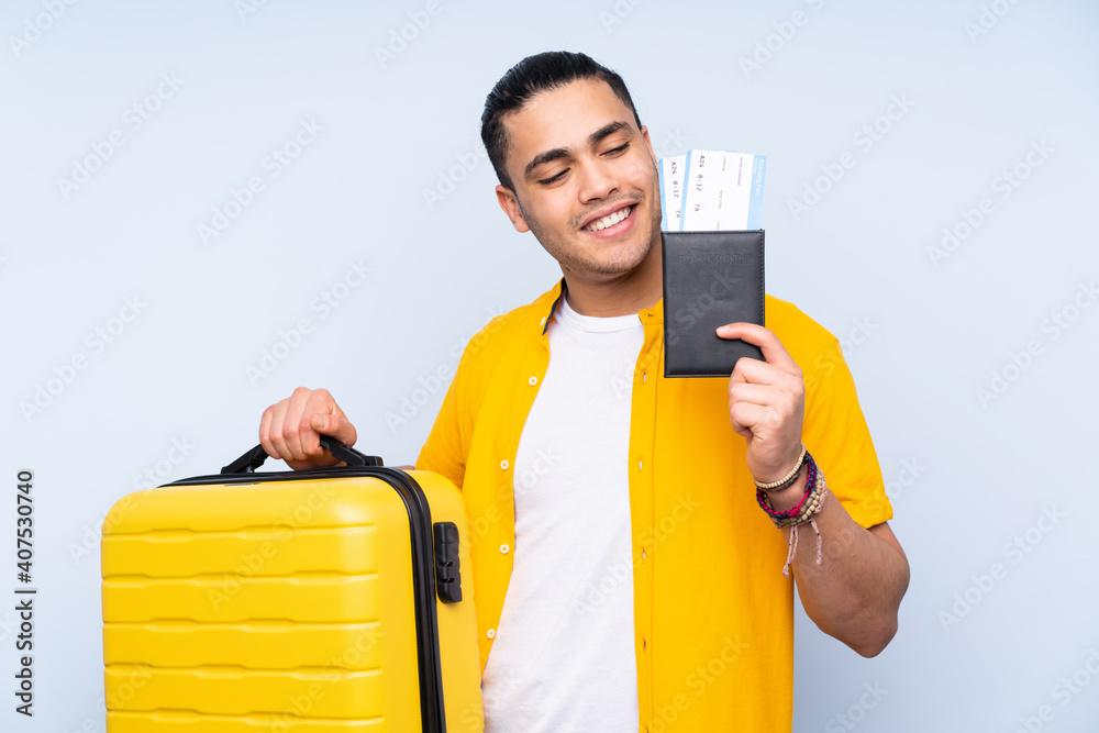Asian handsome man isolated on blue background in vacation with suitcase and passport Asian handsome man isolated on blue background in vacation with suitcase and passport