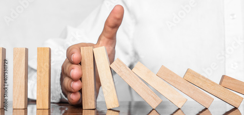 Close-up Of A Human Hand Stopping Wooden Blocks From Falling On Table. The man's hand holds the falling wooden bars. Concept: business, stability, fall, risk, collapse.